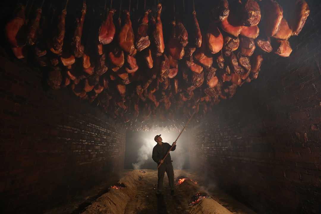 图为腊肉熏制厂房内,工人师傅在浓烟中制作腊肉.